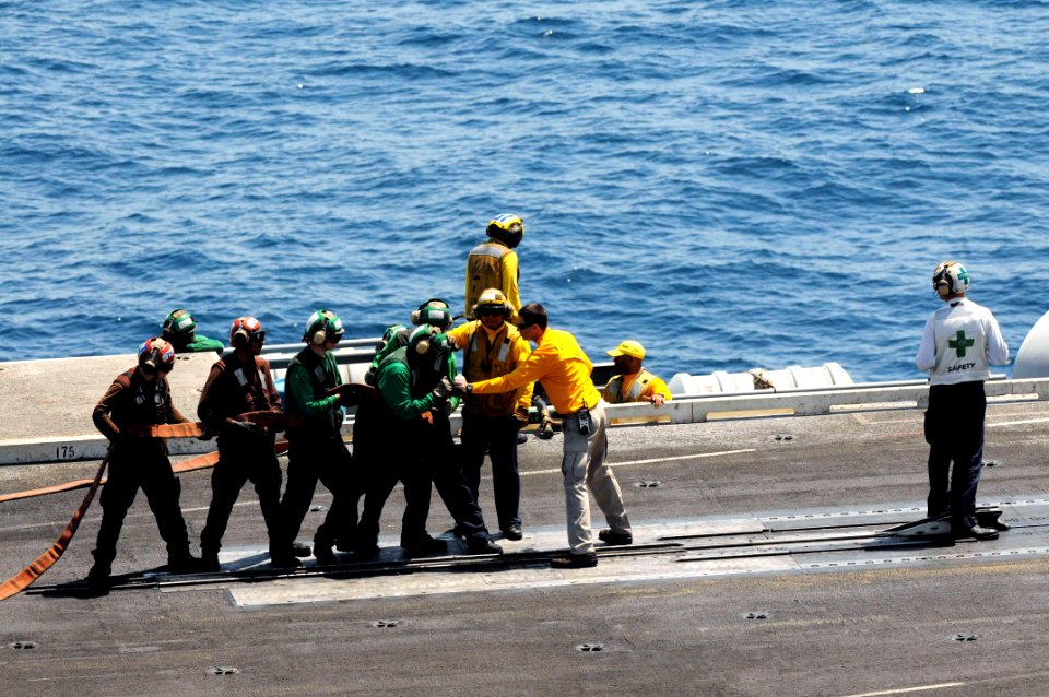 U.S. Navy Chief Aviation Boatswain's Mate (Handling) Shawn Riley, center right, instructs Sailors on proper fire hose handling techniques June 27, 2014, during a general quarters drill on the flight deck of 140627-N-CZ979-049