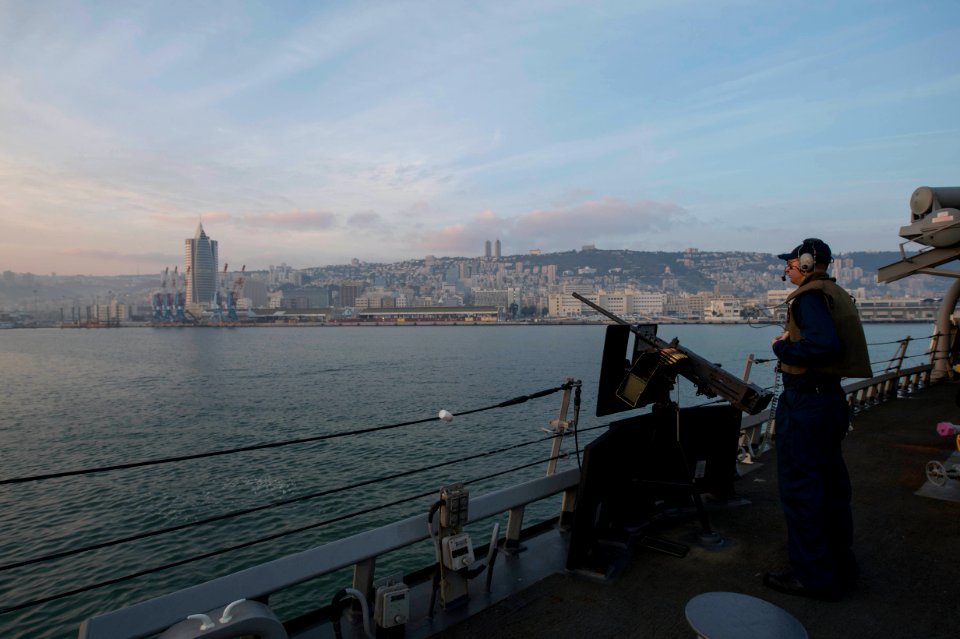 U.S. Navy Fire Controlman 2nd Class Raymond Slaton mans a .50-caliber machine gun aboard the guided missile destroyer USS Stout (DDG 55) as the ship pulls into port in Haifa, Israel, Jan. 19, 2014, for 140119-N-UD469-343