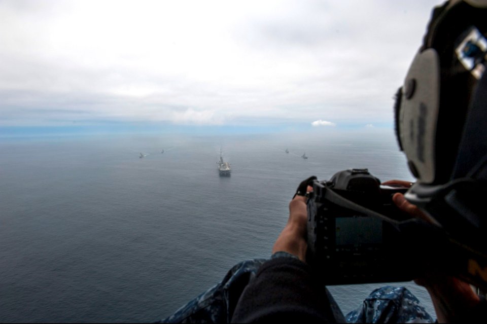 U.S. Navy Mass Communication Specialist 2nd Class Jonathan Colon takes photos of the amphibious assault ship USS America (LHA 6), center, and Peruvian Navy ships as they sail in formation during a passing 140903-N-MZ309-1134