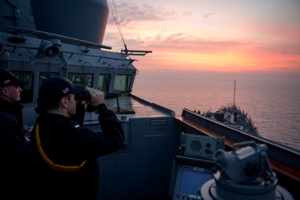 U.S. Navy Lt. j.g. Samuel Braddock, right, looks through binoculars for surface contacts on the bridge wing aboard the guided missile destroyer USS Stout (DDG 55) as the ship prepares to pull into port in Haifa 140119-N-UD469-144