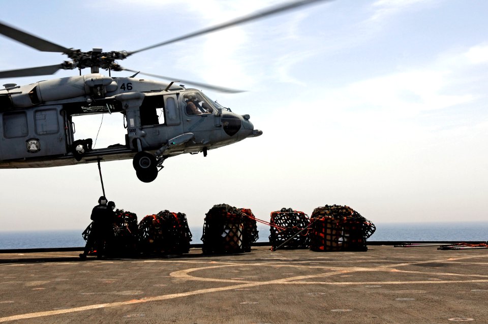 U.S. Navy Logistics Specialist 3rd Class Corey Rainey braces Seaman Naomi Bentley as she connects a cargo pendant to a MH-60S Seahawk helicopter, assigned to Helicopter Sea Combat Squadron (HSC) 23, during 110517-N-RC734-245