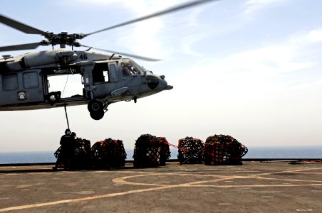 U.S. Navy Logistics Specialist 3rd Class Corey Rainey braces Seaman Naomi Bentley as she connects a cargo pendant to a MH-60S Seahawk helicopter, assigned to Helicopter Sea Combat Squadron (HSC) 23, during 110517-N-RC734-245