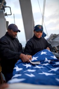U.S. Navy Fire Controlman 2nd Class Cedric Bussey, left, and Quartermaster Seaman Recruit Tayler Simpkins fold a U.S. flag aboard the guided missile destroyer USS Stout (DDG 55) as the ship prepares to pull into 140119-N-UD469-288