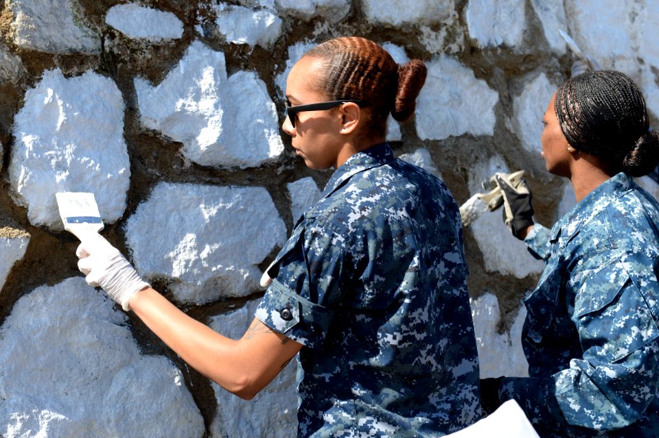 U.S. Navy Seaman Brianna Anderson, left, and Yeoman 1st Class LaDonna Williams, both assigned to the newly commissioned amphibious assault ship USS America (LHA 6), paint an exterior wall at a children's home 140826-N-MZ309-084