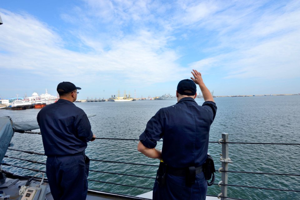 U.S. Navy Logistics Specialist 2nd Class Christopher Younkin, right, waves goodbye aboard the guided missile destroyer USS Ross (DDG 71) as the ship departs Constanta, Romania, Sept 140907-N-IY142-188