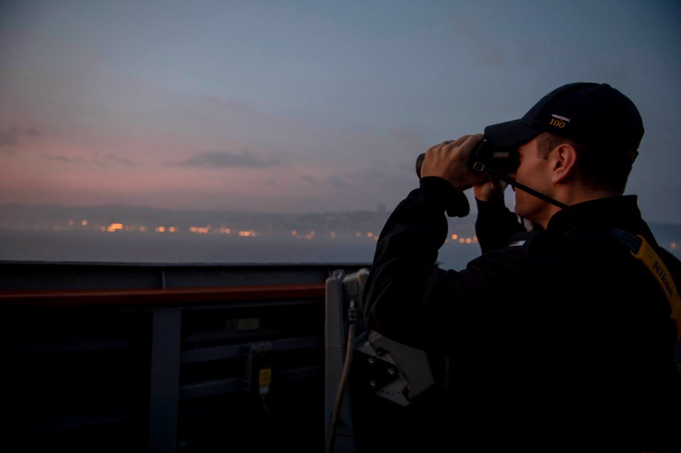 U.S. Navy Lt. j.g. Samuel Braddock looks out binoculars for surface contacts on the bridge wing aboard the guided missile destroyer USS Stout (DDG 55) as the ship prepares to pull into port in Haifa, Israel 140119-N-UD469-115