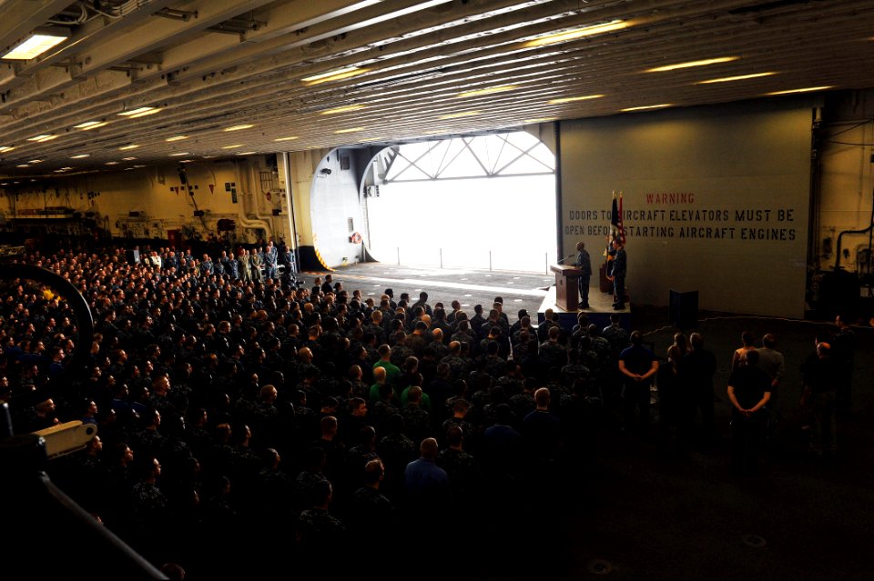 U.S. Navy Rear Adm. Frank L. Ponds, at lectern, the commander of Expeditionary Strike Group 3, gives closing remarks as part of a 9-11 remembrance ceremony in the hangar bay of the newly commissioned amphibious 140911-N-LQ799-155