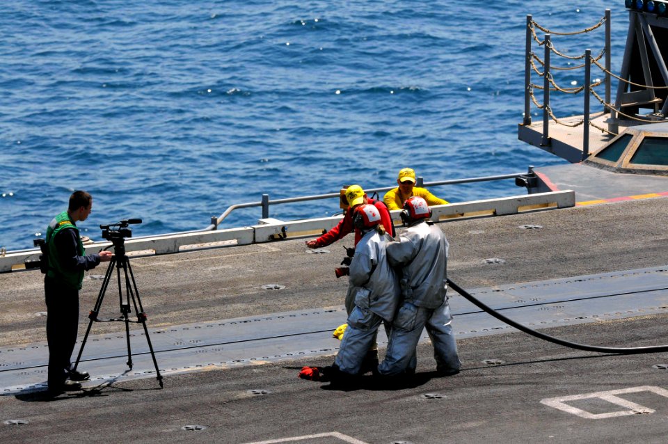 U.S. Navy Mass Communication Specialist 3rd Class Andrew Gordon, left, films Sailors as they learn proper fire hose handling techniques June 27, 2014, during a general quarters drill on the flight deck of 140627-N-CZ979-042