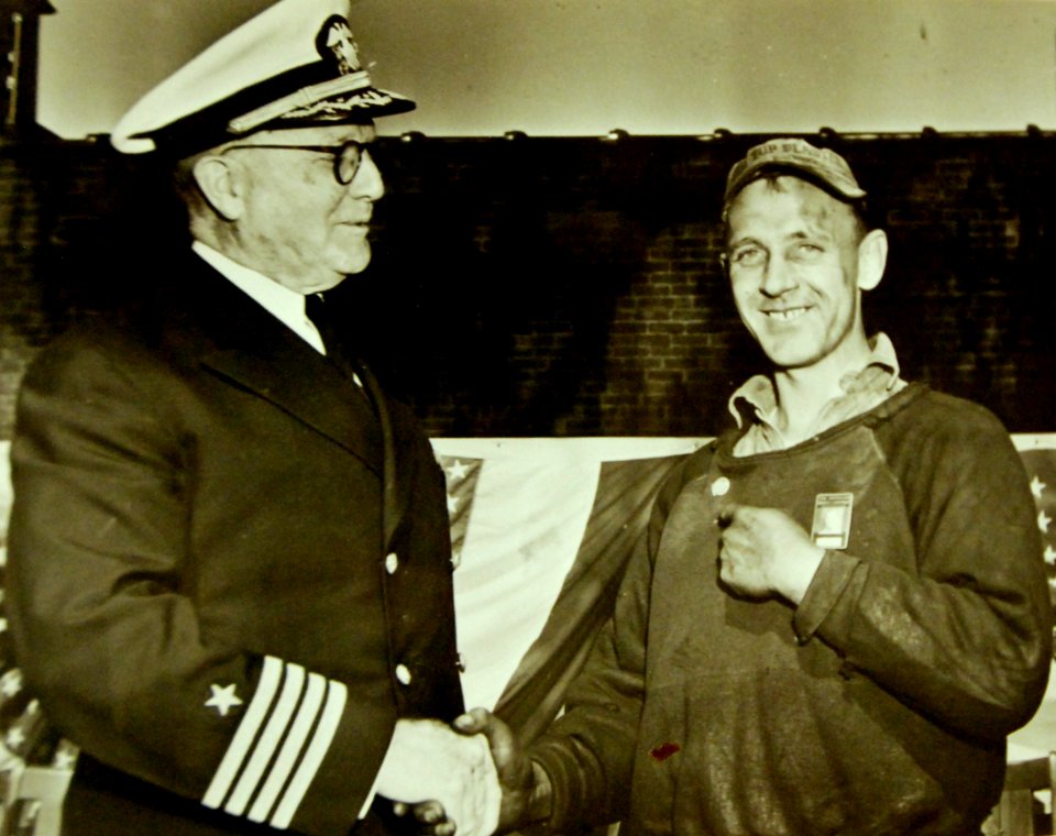 U.S. Navy CPT Robert Henderson presents a Navy “E” button to brass worker Steve Homyak, 1942 (23552276030)
