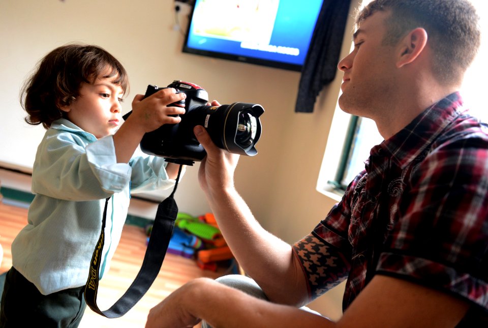 U.S. Navy Mass Communication Specialist 1st Class Corey Green, right, assigned to Commander, Task Force (CTF) 56, shows a little boy his camera during a community relations event at the Regional Institute for 131120-N-OU681-048