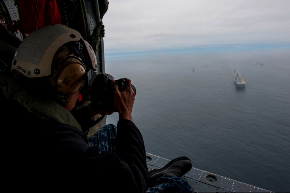 U.S. Navy Mass Communication Specialist 2nd Class Jonathan Colon takes photos of the amphibious assault ship USS America (LHA 6), left, and Peruvian Navy ships as they sail in formation during a passing exercise 140903-N-MZ309-1241