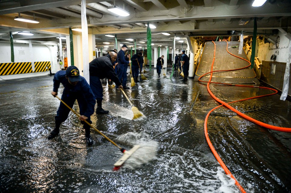 U.S. Sailors aboard the amphibious transport dock ship USS Mesa Verde (LPD 19) sweep away water after a test of aqueous film-forming foam stations during the ship's Board of Inspection and Survey (INSURV) 140116-N-BD629-378