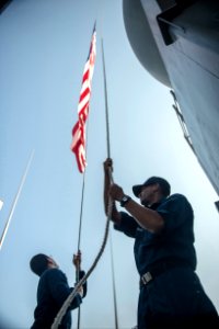 U.S. Navy Seaman Luke Swire, right, lowers an American flag aboard the amphibious transport dock ship USS Denver (LPD 9) after participating in a photo exercise with ships assigned to the Bonhomme Richard 140327-N-ZU025-171