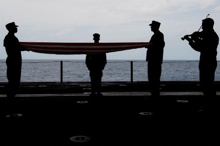 U.S. Navy Lt. j.g. David Kelts, right, plays a violin rendition of Amazing Grace as chief petty officer selects fold the U.S. flag during a 9-11 remembrance ceremony in the hangar bay aboard the newly 140911-N-MD297-004