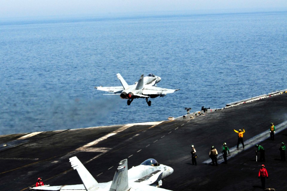 U.S. Sailors prepare to launch an F-A-18C Hornet aircraft attached to Strike Fighter Squadron (VFA) 15 as an F-A-18C Hornet aircraft takes off from the aircraft carrier USS George H.W. Bush (CVN 77) in 140630-N-CZ979-014