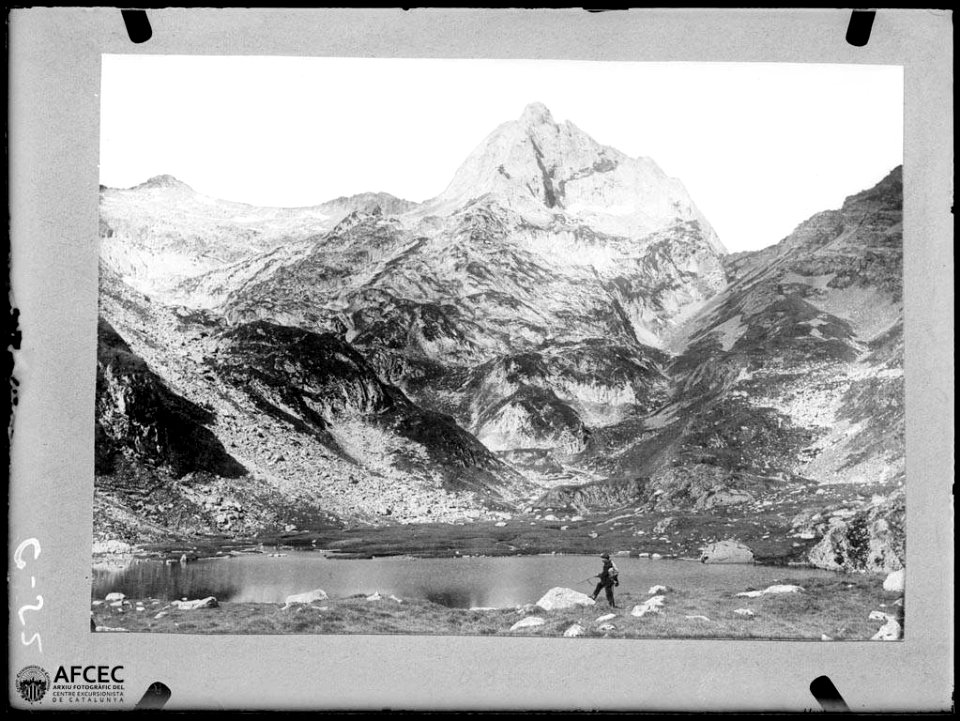 Un alpinista al costat d'un llac i al fons el malh des Pois o Forcanada