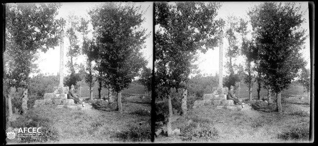 Un excursionista assegut al peu d'una creu de terme amb alguns arbres al voltant a Llobera