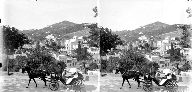 Un cotxe de cavalls en una carretera i més enllà edificis de Vallcarca