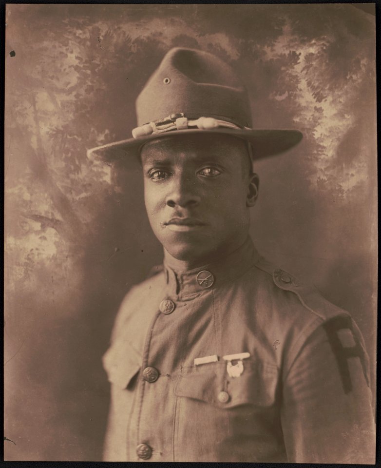 Unidentified African American soldier in uniform with First Army shoulder insignia and campaign hat in front of painted backdrop LCCN2017648713