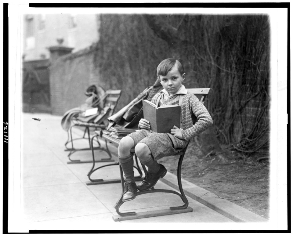 Unidentified boy, seated on park bench, probably in Washington, D.C., holding book LCCN94506123