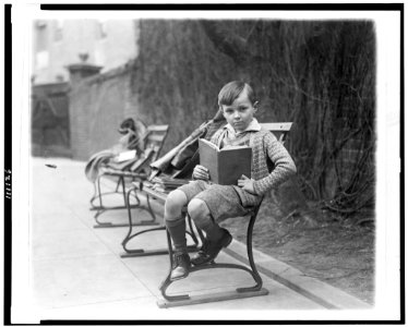 Unidentified boy, seated on park bench, probably in Washington, D.C., holding book LCCN94506123