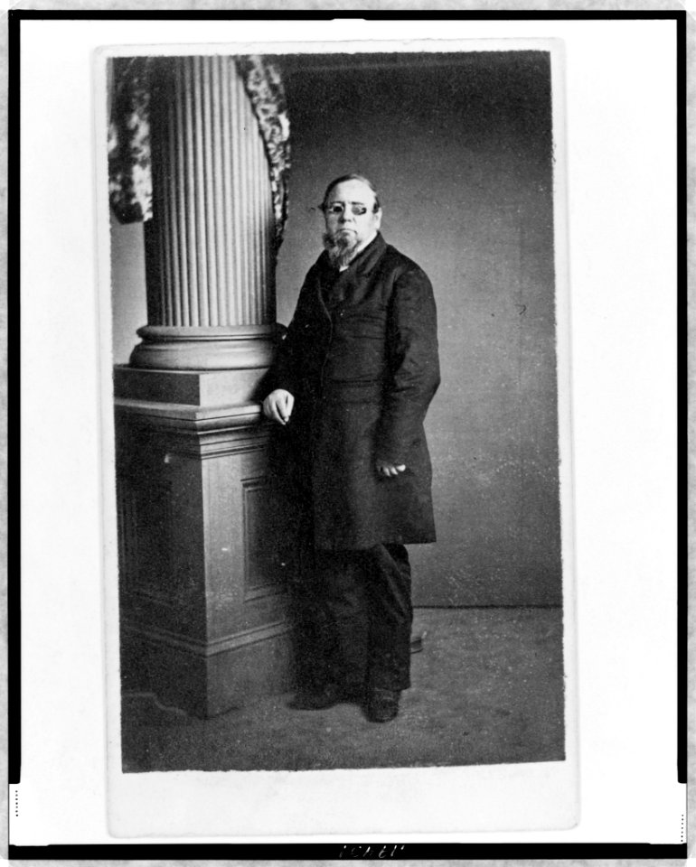 Unidentified man, full-length portrait, wearing spectacles with colored lenses, standing next to column, facing left LCCN98506729