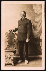 Unidentified man, facing front, standing next to chair, posing for full-length studio portrait LCCN2015649998