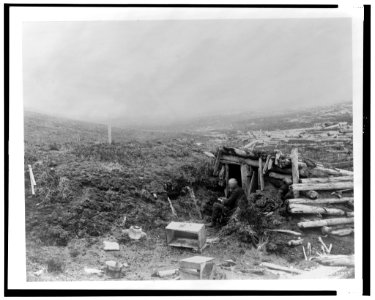 Unidentified old man, seated, writing, at entrance to a log and earth shelter in Alaska, 1899) - Curtis LCCN2002706851