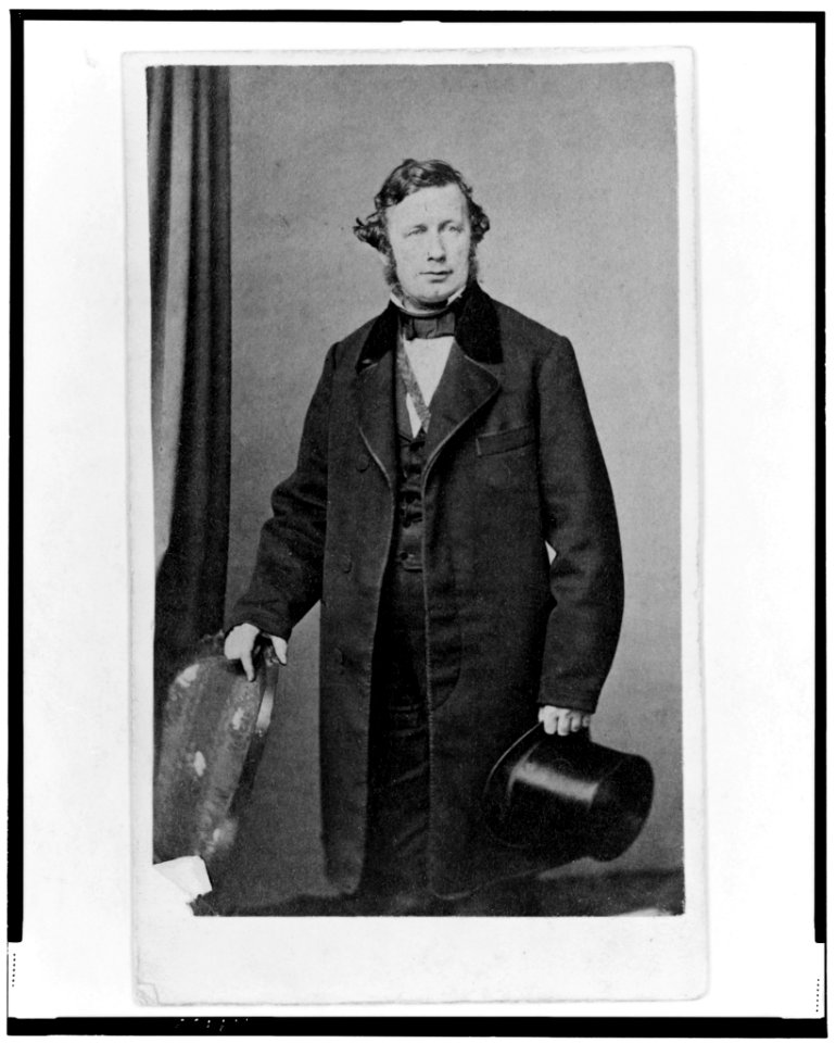 Unidentified man, three-quarter length portrait, standing, posed slightly to the left with right hand on back of chair, holding top hat in left hand LCCN98506732