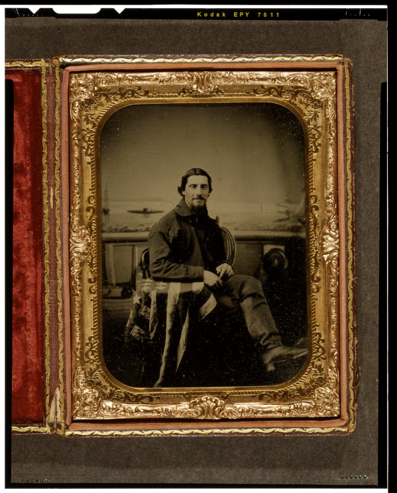 Unidentified sailor seated in front of a painted backdrop showing nautical scene, right arm resting on table draped with an American flag LCCN2004672440