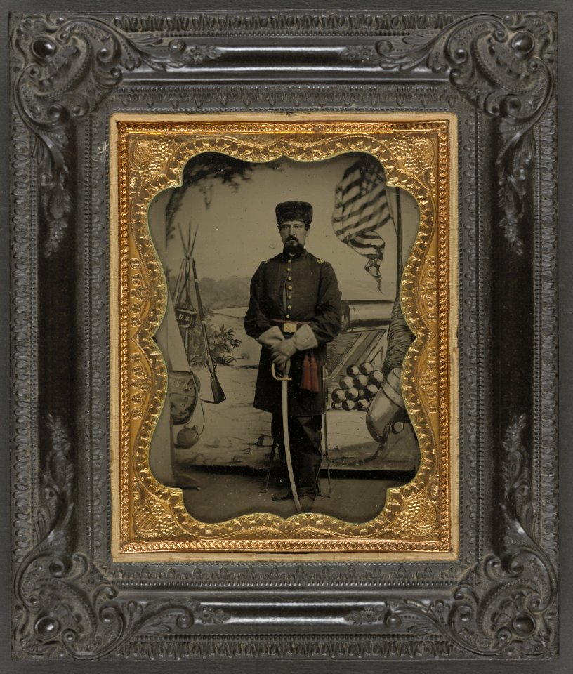 Unidentified soldier in Union uniform with sword in front of painted backdrop showing weapons and American flag at Benton Barracks, Saint Louis, Missouri LCCN2012648269