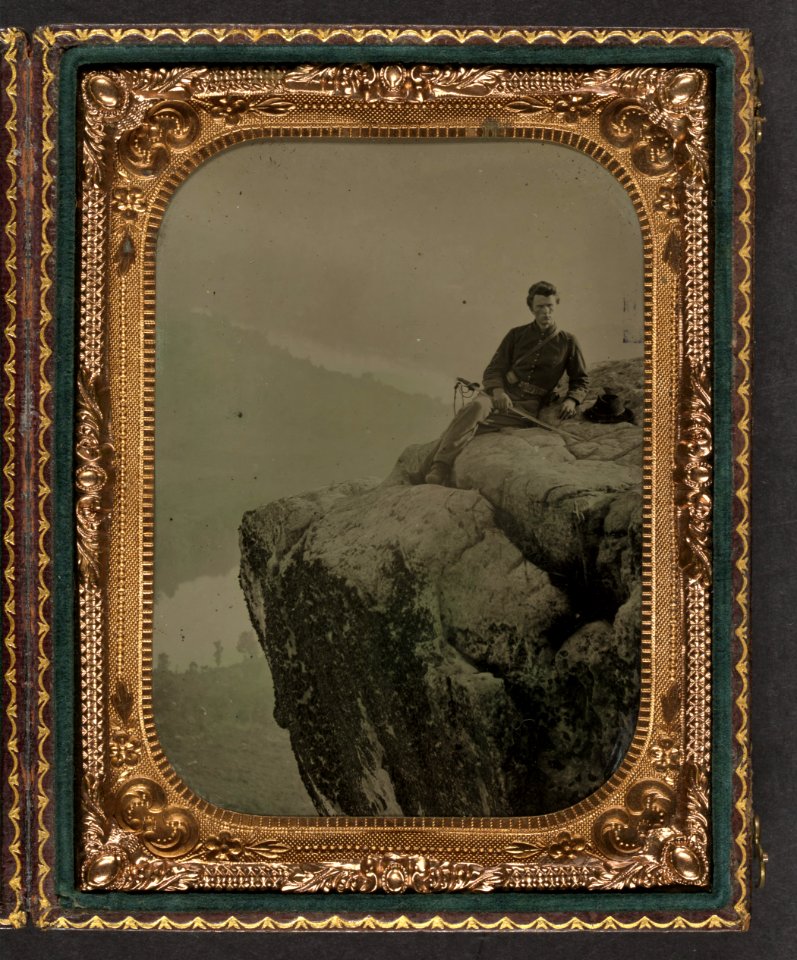 Unidentified soldier in Union officer's uniform at Point Lookout, Tennessee, sitting with cavalry saber in hand and slouch hat resting beside him on a rock LCCN2010648878