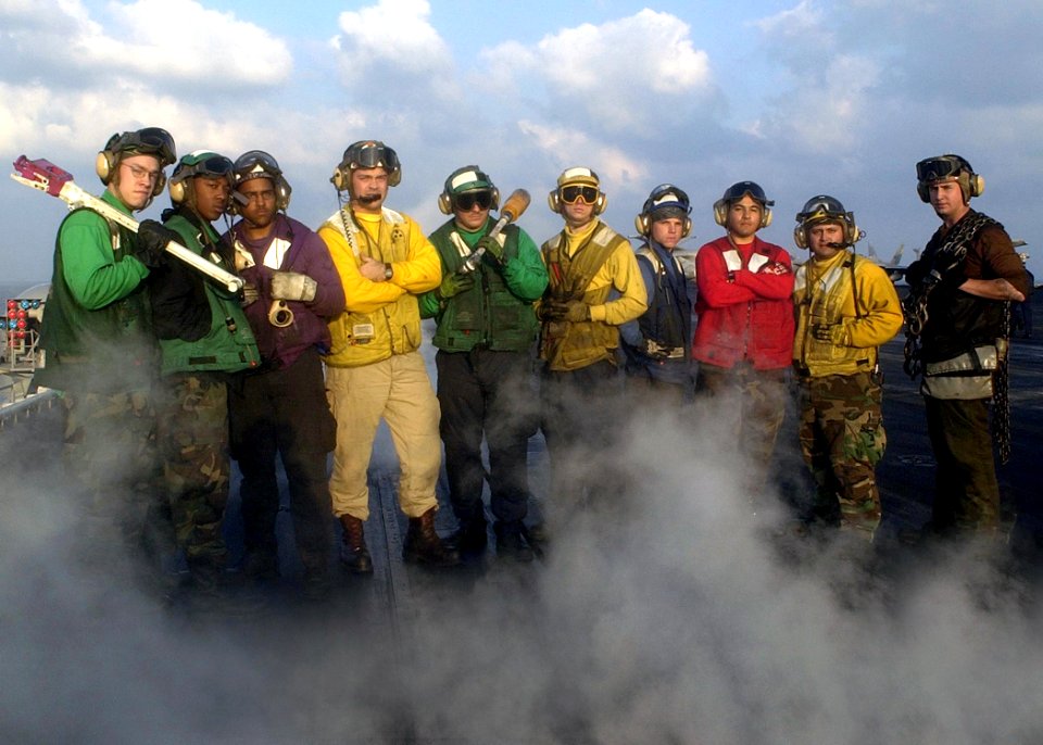 US Navy 030106-N-4142G-004 Flight deck crewmembers pose on one of four steam driven catapults after launching numerous flight missions, on the ship's flight deck