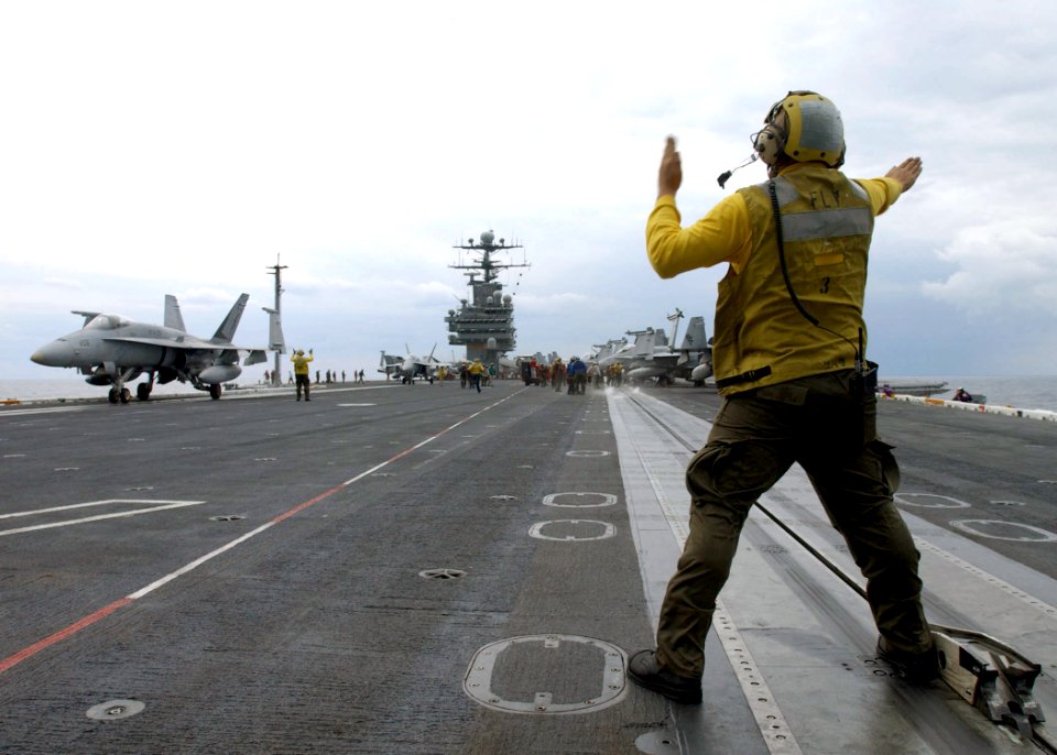US Navy 021209-N-6895M-503 plane director guides an F-A-18 into position on the ship's flight deck