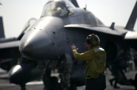 US Navy 021225-N-4142G-010 A flight deck director moves an F-A-18 Hornet into position as it prepares to launch one of four steam driven catapults on the ship's flight deck