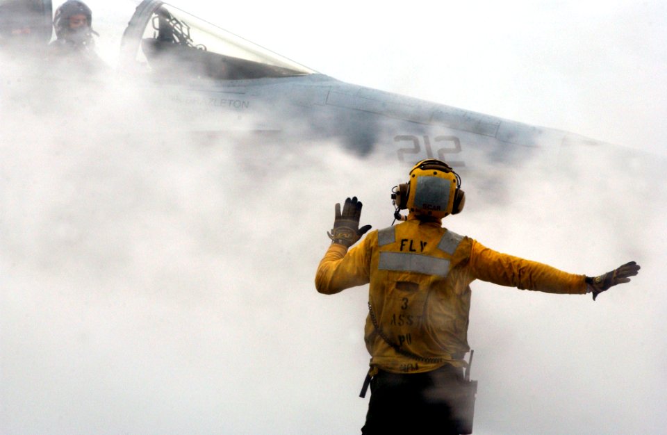 US Navy 021213-N-6895M-507 A flight deck director guides an F-A-18 Hornet from the Hunters of Strike Fighter Squadron Two Zero One (VFA-201) through steam from one of four steam driven catapults on the ship's flight deck