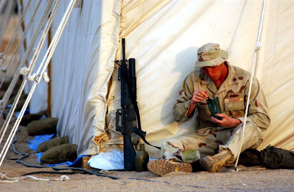 US Navy 030208-N-5319A-002 Builder 2nd Class Nathan Waite assigned to Naval Mobile Construction Battalion Seventy-Four (NMCB-74) eats a Meal Ready to Eat (MRE) outside his 60-man berthing tent