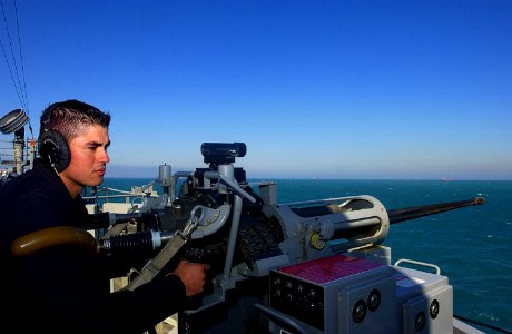 US Navy 030302-C-9409S-006 Seaman Juan Macias mans a 25 mm machine gun aboard the amphibious dock landing ship USS Comstock (LSD 45) keeping an eye out for a possible attack against the ship