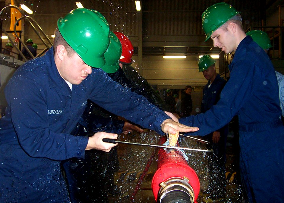 US Navy 030226-N-1711I-001 Aviation Ordnanceman Airman Recruit Brian Gonzales from San Jose, Calif., saws a wooden wedge to plug a broken pipe during a wet-trainer exercise