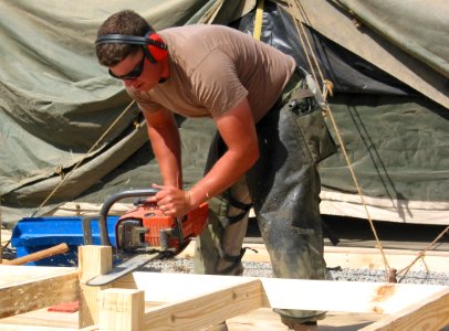 US Navy 030318-N-1050K-002 Steelworker 3rd Class Mike Freeman from Northern Hills, Calif., trims the excess off of the flooring frame during tent strong-backing efforts