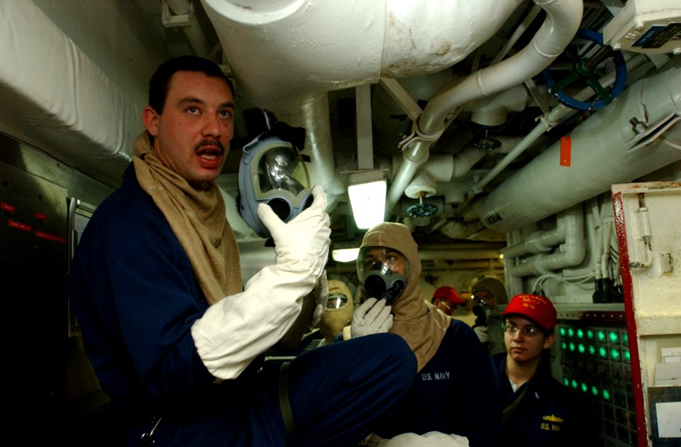 US Navy 030227-N-6141B-003 Damage Controlman Fireman Apprentice Chad Forcht from St. George, Utah, instructs crewmembers on the proper use of the MCU-2P gas mask during a chemical, biological, and radiological training aboard t