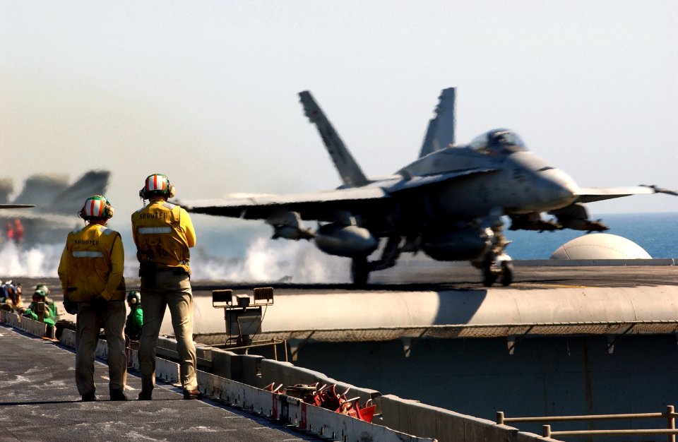 US Navy 030402-N-1810F-003 An F-A-18C Hornet launches past onlooking shooters located at the bow of USS Kitty Hawk (CV 63)