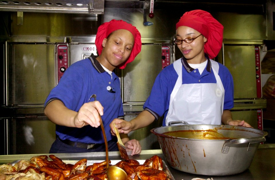US Navy 030326-N-2143T-001 Mess Management Specialist 3rd Class Andrea Yepez from Saginaw, Mich., and Mess Management Specialist Seaman Lene Jones from Alexandra, La., prepare barbecued chicken for the more than 5,000 Sailors a