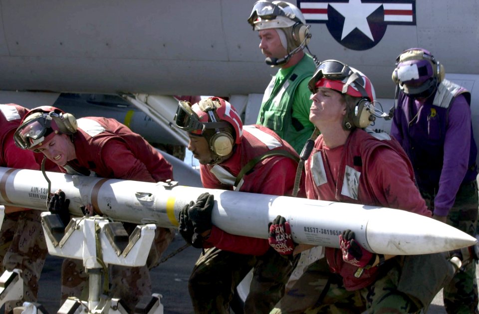 US Navy 030418-N-2385R-011 Aviation Ordnanceman lift an AIM-120 Advanced Medium-Range Air-to-Air Missile (AMRAAM) from its weapon skid to load it onto an F-A-18C Hornet