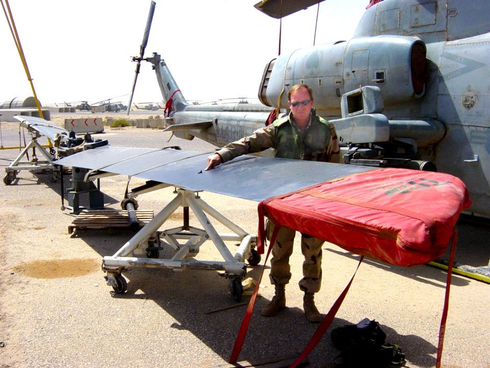 US Navy 030410-N-0000Z-001 Naval Air Systems Command Depot Cherry Point Planner and Estimator Mike Day points toward a bullet hole in the rotor blade of a helicopter
