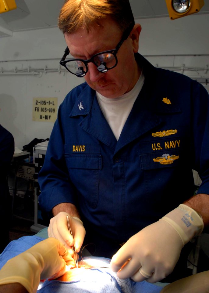 US Navy 081201-N-2456S-026 Capt. Tom Davis applies sutures to a patient's face after removing a facial mass