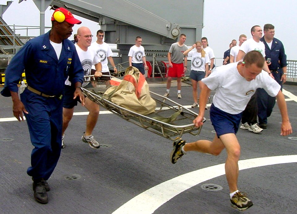 US Navy 030610-N-0000X-023 Lt. Atkins Jinadu (left) runs alongside a team of three midshipmen competing in a Damage Control Olympics relay, an event which gives the midshipmen hands on experience with damage control situations
