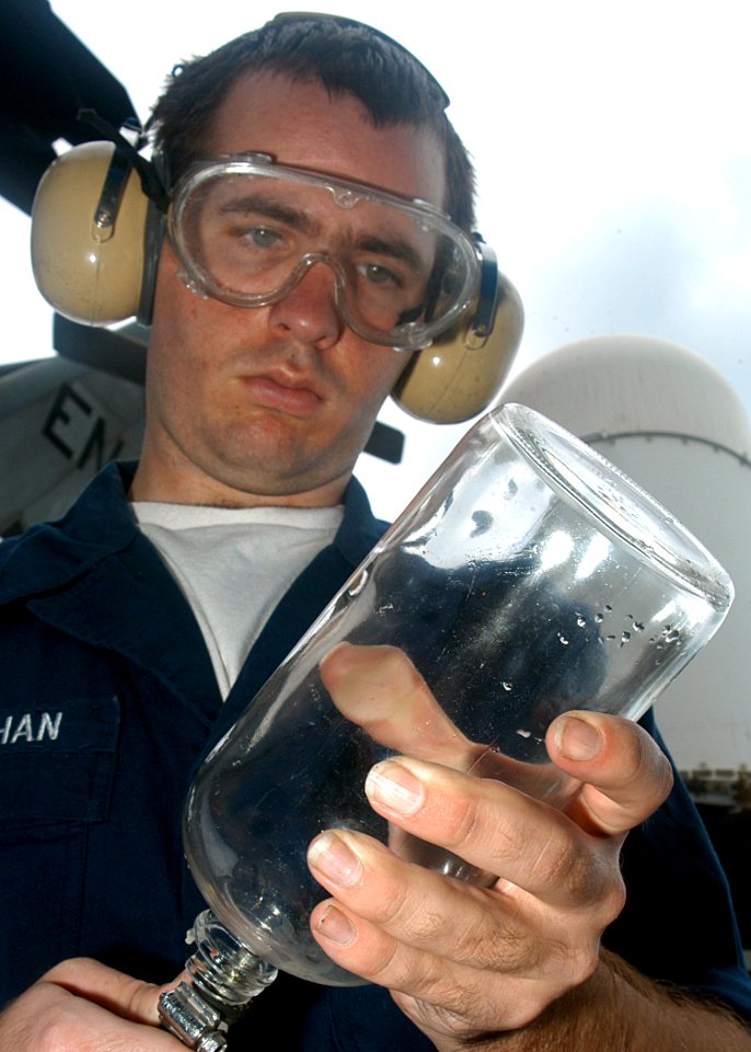 US Navy 030618-N-2972R-068 Aviation Boatswain's Mate Airman David Monahan, from Boston, Mass., uses low-pressure air to dry a JP-5 fuel sample bottle after cleaning it