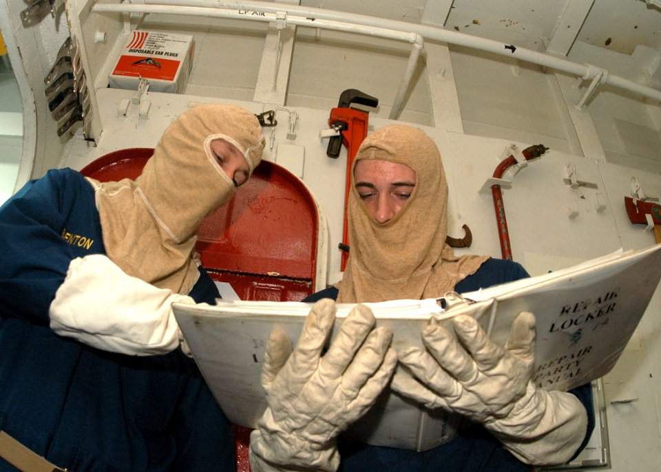 US Navy 031014-N-8955H-003 Chief Information Systems Technician Joseph Benton, from New Orleans, La., and Ensign Brent Zito, from Jonesboro, Ark., read instructions for combating a main space fire