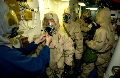US Navy 030920-N-5471P-004 Damage Controlman 3rd Class Michael Muskett helps Ship's Serviceman 3rd Class Daniel Olaya don chemical protective gear